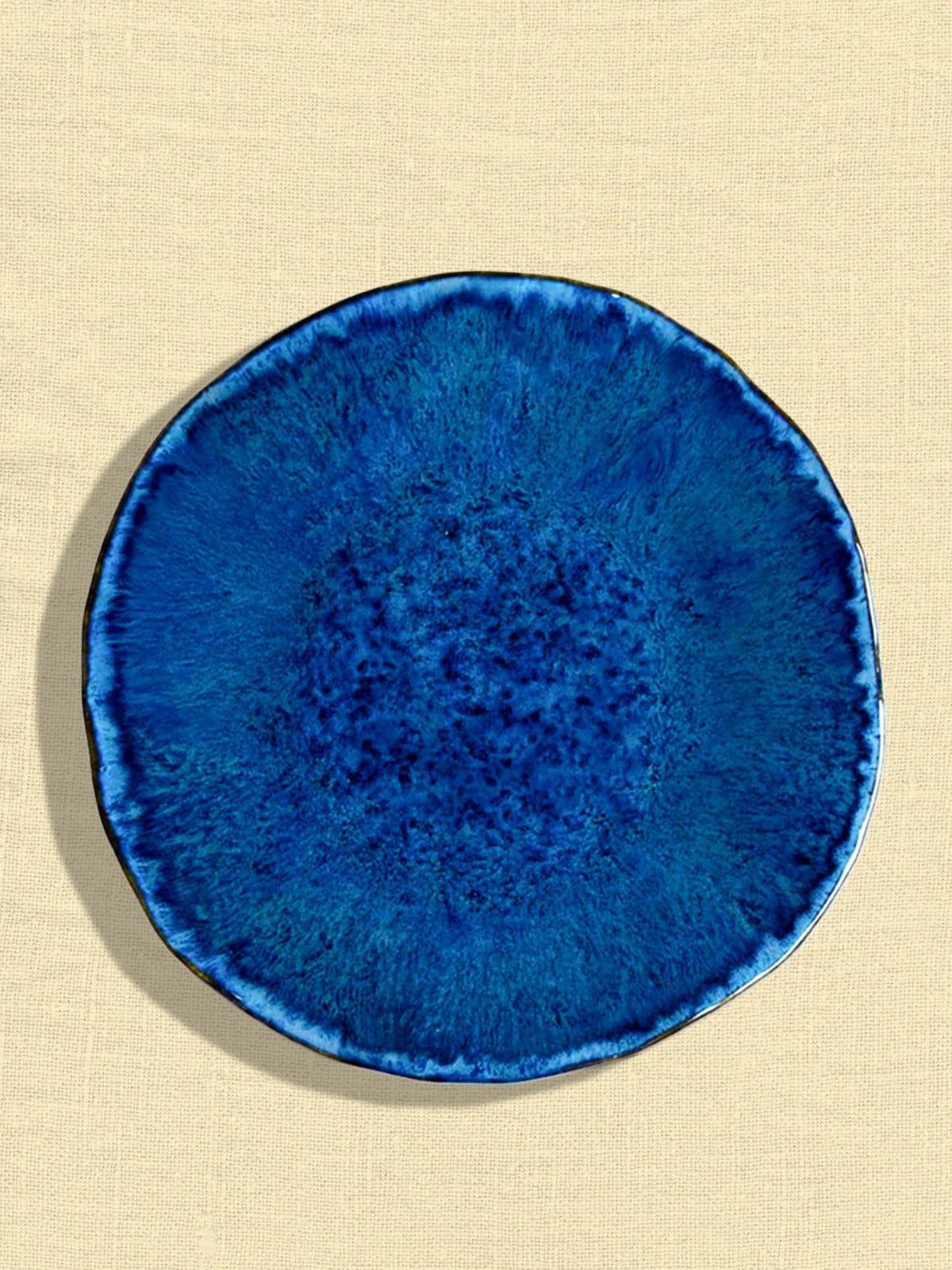Grande assiette Onda en céramique émail bleu abyssal Céladon, sur fond coloré