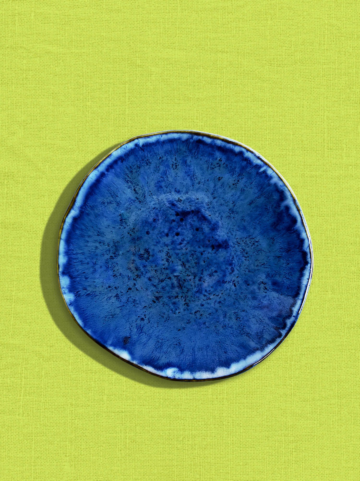 Petite assiette Onda en céramique émail bleu abyssal Céladon, sur fond coloré